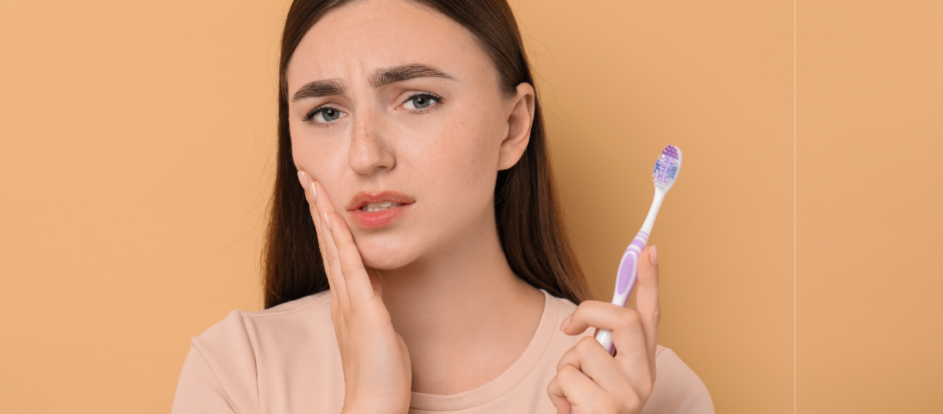 gengivas e hormonas: mulher com a mão na face e uma escova de dentes na mão